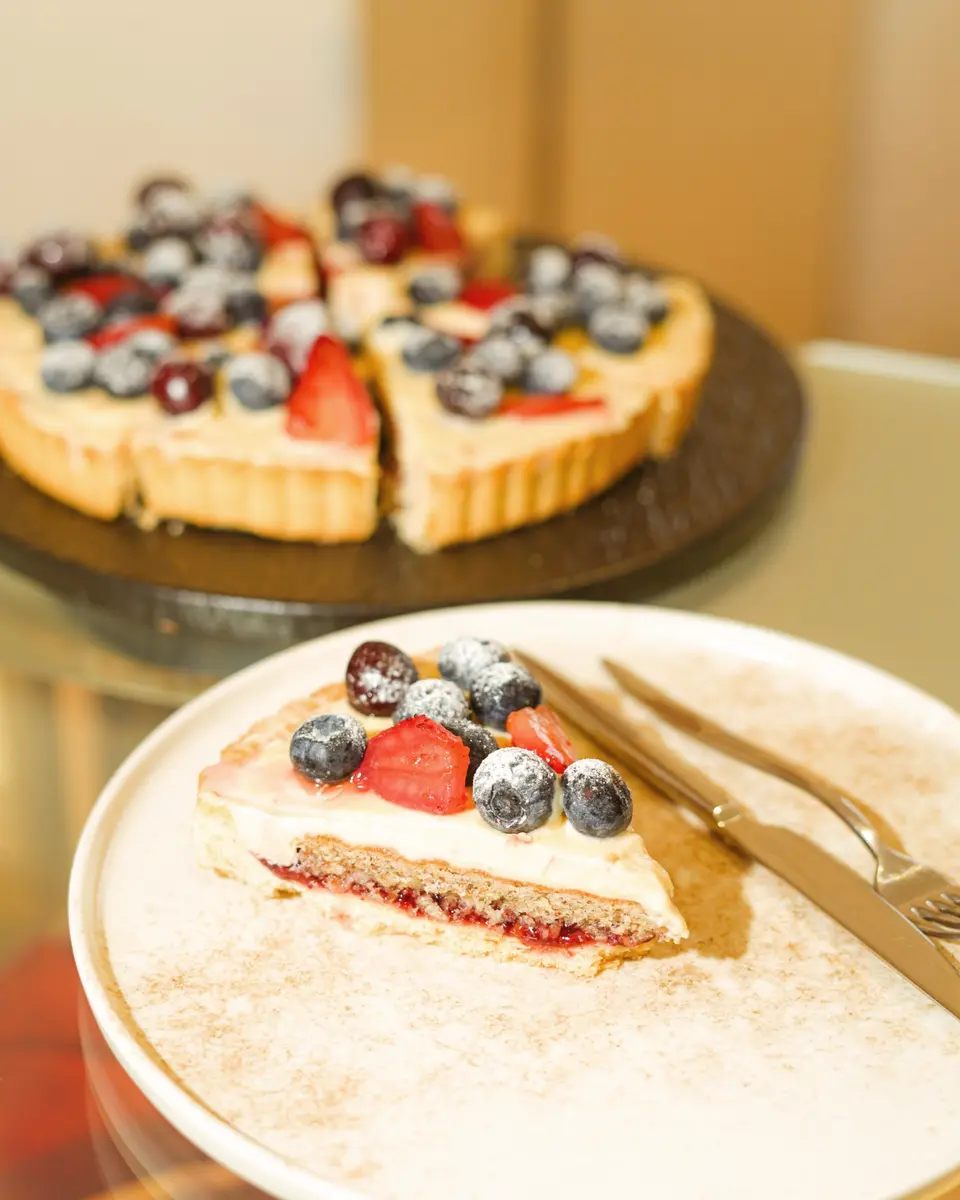 Slice of Lamoge berry tart with cream, strawberry, and blueberries